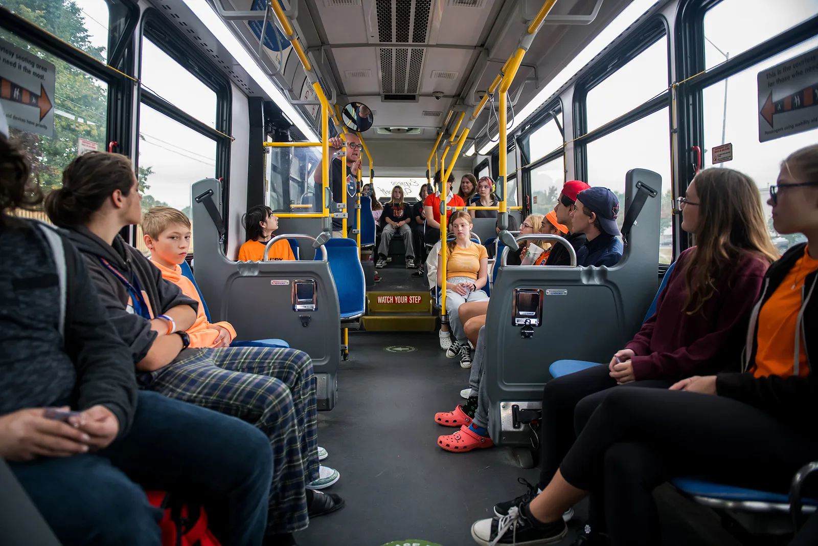 Students seated aboard a Get on the Bus transit tour bus, mid-conversation with the program's director.