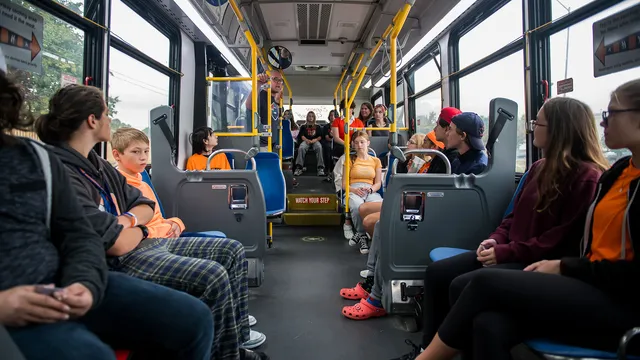 Students seated aboard a Get on the Bus transit tour bus, mid-conversation with the program's director.