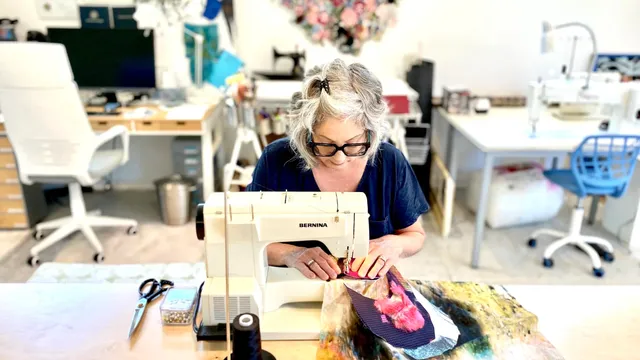 Wild Bobbin's Kingston studio, a sewing instructor working at a machine surrounded by workshop tables and supplies.